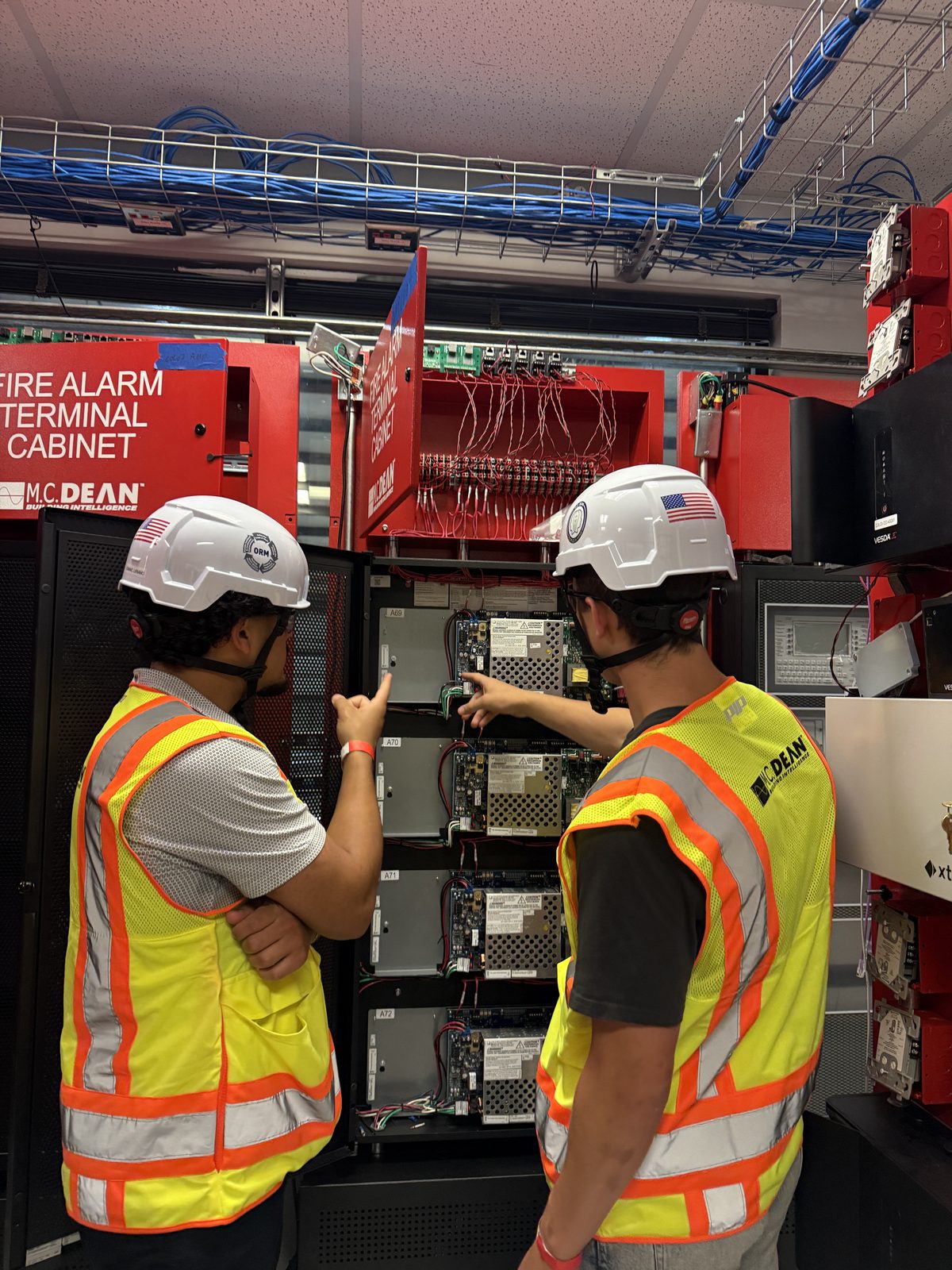 Reviewing power supplies inside a fire alarm terminal cabinet with a colleague